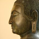 Side profile of a bronze Buddha statue with serene expression.